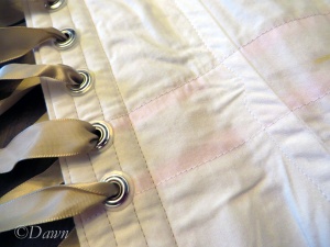 Inside close up of the white silk overbust corset showing the grommets, ribbon, and the slight pink of the waist stay